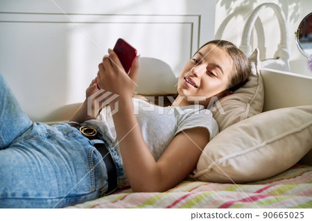 Beautiful young teenage female resting lying on couch using smartphone Beautiful young teenage female resting lying on couch using smartphone 90665025