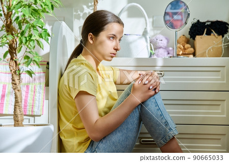 Sad teenage girl sitting on the floor at home Sad teenage girl sitting on the floor at home 90665033