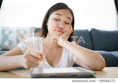 Happy Asian young woman relaxing in the living room and watching a contents and chatting with her friends and drawing an illustration on tablet. Woman enjoy watching video and drawing on tablet. Happy Asian young woman relaxing in the living room and watching a contents and chatting with her friends and drawing an illustration on tablet. Woman enjoy watching video and drawing on tablet. 90669272