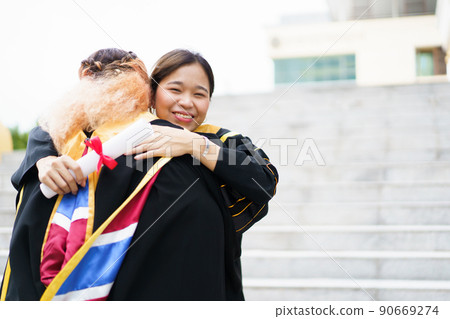 Happy Asian young women in the master degree gown showing a diploma in their hand close up. Portrait of confident college students in gown in the graduation ceremony. 90669274