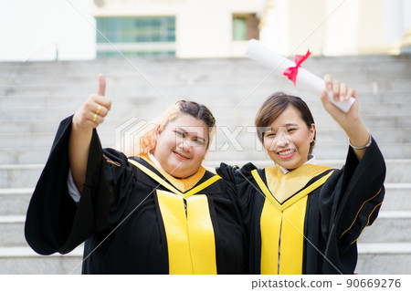 Happy Asian young women in the master degree gown showing a diploma in their hand close up. Portrait of confident college students in gown in the graduation ceremony. 90669276