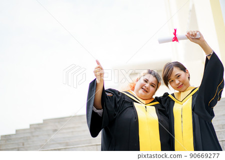 Happy Asian young women in the master degree gown showing a diploma in their hand close up. Portrait of confident college students in gown in the graduation ceremony. 90669277