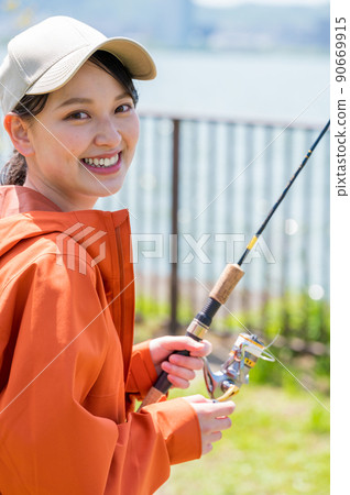 A smiling young woman enjoying fishing as a hobby under the blue sky A smiling young woman enjoying fishing as a hobby under the blue sky 90669915