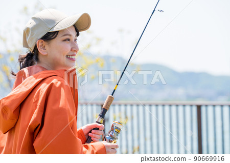 一個微笑的年輕女子在藍天下享受釣魚作為一種愛好 90669916