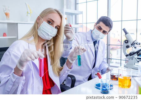 Two scientists wears hygiene protective mask are working holding looking at test tube with sample in a chemistry lab scientist are doing investigations in Laboratory analysis background 90672235