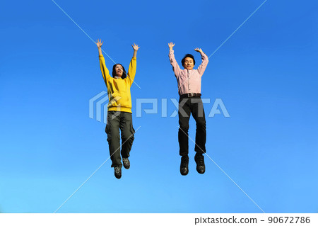 A senior couple who raises both hands and jumps vigorously against the background of the blue sky 90672786