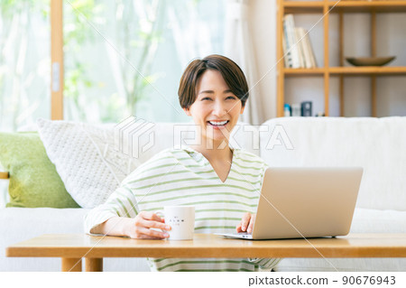 Middle-aged woman looking at a computer in the living room Middle-aged woman looking at a computer in the living room 90676943