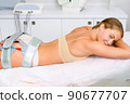 A beautiful woman lies on a couch during an electromyostimulation procedure. 90677707