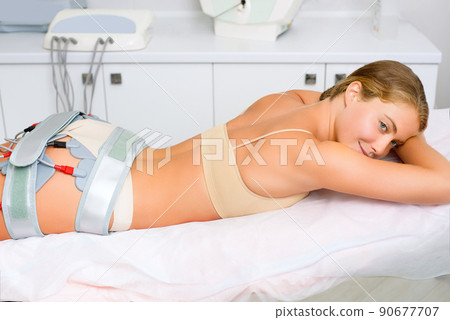 A beautiful woman lies on a couch during an electromyostimulation procedure. A beautiful woman lies on a couch during an electromyostimulation procedure. 90677707