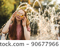 Young beautiful red-haired long-haired woman in a summer pink dress walks through the streets of a summer city. 90677966