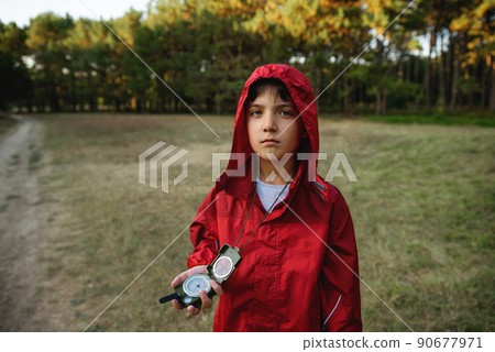 A boy in a red windbreaker against the backdrop of a forest with a compass in his hand. 90677971