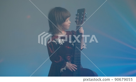 Cute little girl stands on stage in vintage dress and plays an acoustic guitar like a counter bass or cello. The concept of performing the author jazz and blues music. Hobbies and art among children Cute little girl stands on stage in vintage dress and plays an acoustic guitar like a counter bass or cello. The concept of performing the author jazz and blues music. Hobbies and art among children 90679055