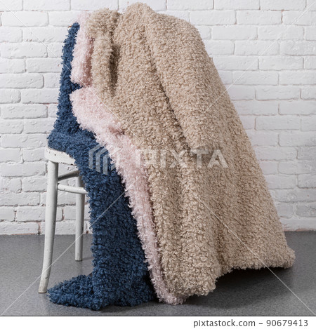 three faux fur coats, blue, beige and pink, laid out on the back of a chair against a white brick wall three faux fur coats, blue, beige and pink, laid out on the back of a chair against a white brick wall 90679413