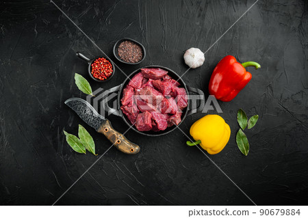 Beef stew prepared for goulash cooking with sweet bell pepper, in cast iron frying pan, on black stone background, top view flat lay, with copy space for text Beef stew prepared for goulash cooking with sweet bell pepper, in cast iron frying pan, on black stone background, top view flat lay, with copy space for text 90679884