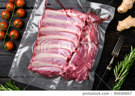 Raw frenched rack of lamb organic meat in sealed plastic wrapping, on black wooden table background, top view flat lay 90680667