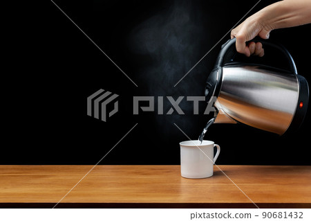 pouring water from kettle water boiler into a cup with smoke on wood table and black background 90681432