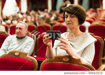 woman takes picture of performance with his phone in theater hall woman takes picture of performance with his phone in theater hall 90682019