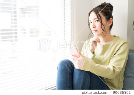A woman operating a smartphone by the window 90686501