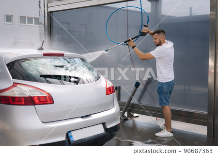 Back view of young man cleaning his car with a jet sprayer. Self service car washing Back view of young man cleaning his car with a jet sprayer. Self service car washing 90687363