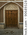 Wooden double-leaf door with an oval brick frame on the facade of an adobe house along a narrow street  of the ancient city of Yazd. 90689328