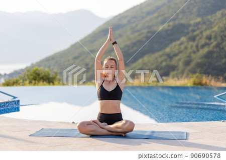 Young fitness woman doing her morning yoga routine at the open air near the pool. 90690578