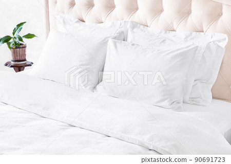Bedroom with bed, white bedding, and bedside table. White pillows, duvet and duvet case on bed with beige headboard. 90691723