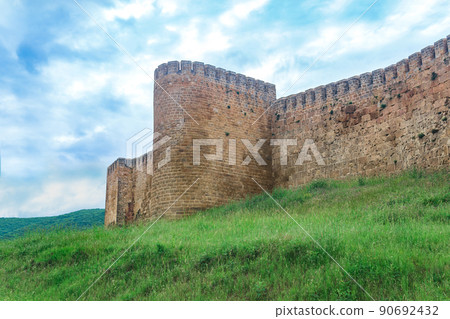 wall of a medieval fortress above a rampart overgrown with grass against the hills and sky, Naryn-Kala citadel in Derbent 90692432