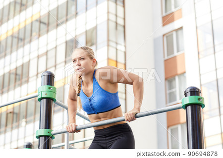 Motivated young woman in sportswear breathing out while doing chin-up exercise at workout area by house 90694878