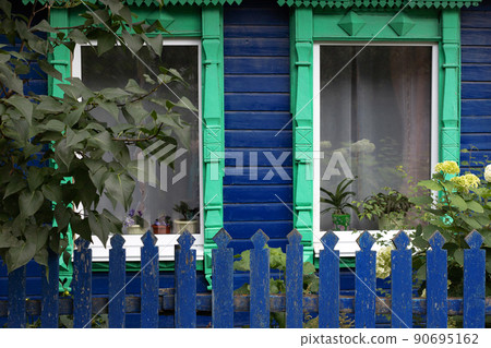 Green carved platband windows with curtains of old traditional russian painted blue wooden house Green carved platband windows with curtains of old traditional russian painted blue wooden house 90695162