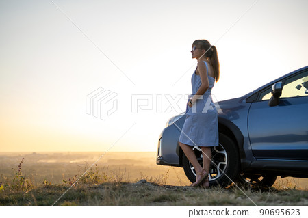 Young female driver resting near her car enjoying warm summer evening. Travel and getaway concept. 90695623