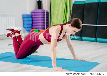 a slender sports woman in a burgundy tracksuit exercises on a mat a slender sports woman in a burgundy tracksuit exercises on a mat 90696617