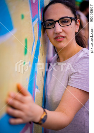 Young and beautiful woman leans against a colorful wall and poses for the camera - typical street 90698697