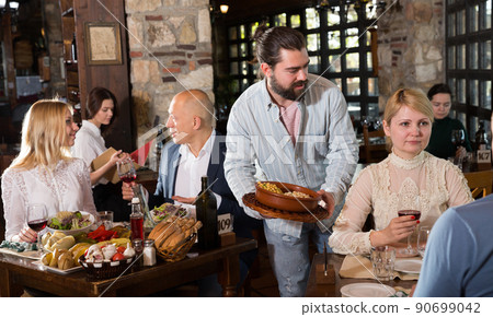 Waiter placing order in front of guests in country restaurant Waiter placing order in front of guests in country restaurant 90699042