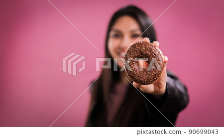 Young Woman holds a chocolate doughnut to the camera 90699043