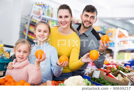 Happy family with two little girls looking for fresh oranges in supermarket Happy family with two little girls looking for fresh oranges in supermarket 90699257
