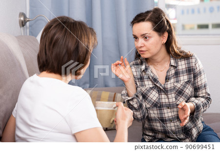 Smiling young female friends gossiping on sofa in home interior 90699451