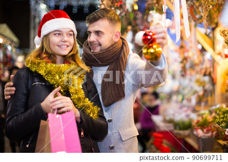 Joyful couple in Christmas hat with Christmas toys at fair Joyful couple in Christmas hat with Christmas toys at fair 90699711
