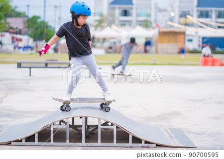 Child or kid girl playing surfskate or skateboard in skating rink or sports park at parking to wearing safety helmet elbow pads wrist and knee support 90700595