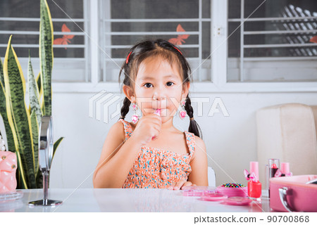 little girl making makeup her face she look in the mirror and applying red lipstick to mouth 90700868