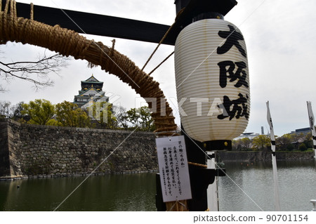 日本春天的大阪城、盛開的櫻花和宏偉的城堡塔、在護城河中運營的船屋的入口門、傳統的燈籠裝飾 90701154