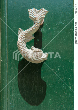 Close-up view of the fish shaped knocker on a green wooden door 90703764