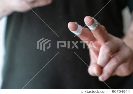 Close-up of a man's hand showing a gesture of victory. White armbands on pointer and middle finger of adult man's hand. . Selective focus. Close-up of a man's hand showing a gesture of victory. White armbands on pointer and middle finger of adult man's hand. . Selective focus. 90704944