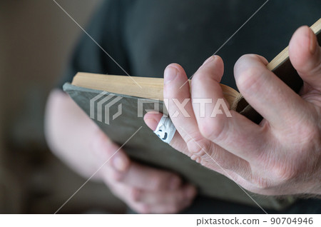 A man is reading a book while holding it in his hands. The first phalanx of his pinky finger is wrapped in white ribbon. A smiling face is painted on the bandage. A man is reading a book while holding it in his hands. The first phalanx of his pinky finger is wrapped in white ribbon. A smiling face is painted on the bandage. 90704946