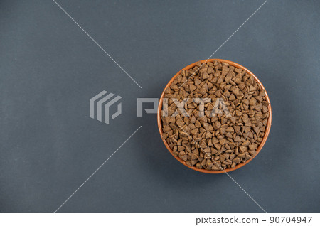 A full bowl of cat food against a gray background. Triangular-shaped pellets in a round clay bowl. Food for senior cats. Useful food for pets concept. Copy space for text and whether design elements. A full bowl of cat food against a gray background. Triangular-shaped pellets in a round clay bowl. Food for senior cats. Useful food for pets concept. Copy space for text and whether design elements. 90704947