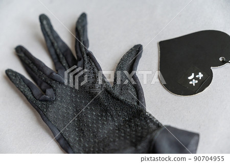 A black lace glove and a paper heart against a gray background. A sad face with crosses over the eyes is drawn in white marker on the heart. Unrequited love, loss of a loved one concept. A black lace glove and a paper heart against a gray background. A sad face with crosses over the eyes is drawn in white marker on the heart. Unrequited love, loss of a loved one concept. 90704955