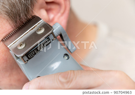 A mature man gets his hair cut. A man cuts his hair with a haircutting clipper. Haircutting sideburns. Close-up. Selective focus. 90704963