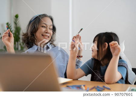 Happy senior grandma and cute little kid granddaughter watching cartoons on laptop together, happy older grandmother grawing and painting. 90707601