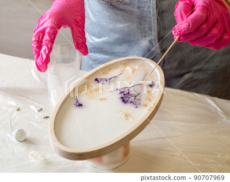 The art process of pouring epoxy resin into a wooden toy. Technology process of creating a painting in style resin art, works with epoxy in studio, makes a wooden stand with the image. Close up. 90707969