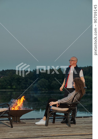 Couple watches the sunset sitting by the fire on the pier 90709145