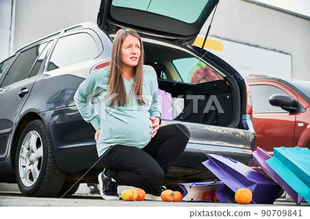 Caucasian pregnant woman waiting for ambulance during premature childbirth at car parking in city. Mother with paper bags feeling pain in belly abdomen have birth contractions after shopping time 90709841